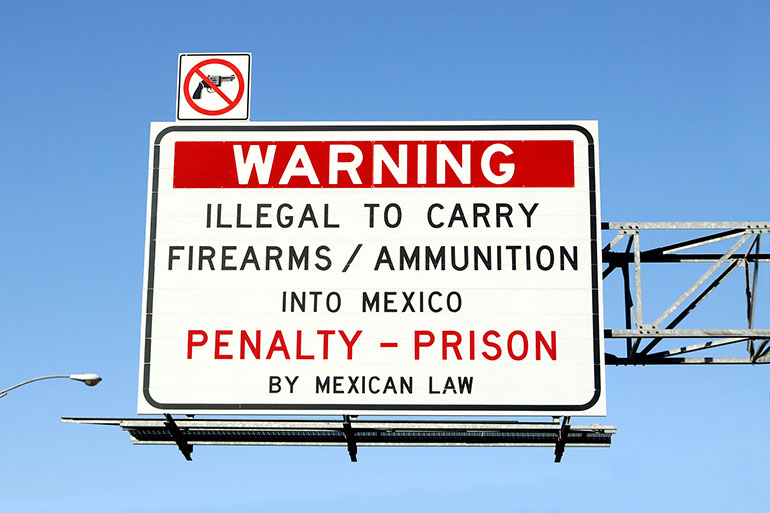 Warning sign above road urging travelers not to carry firearms and ammunition across to border from the U.S. to Mexico