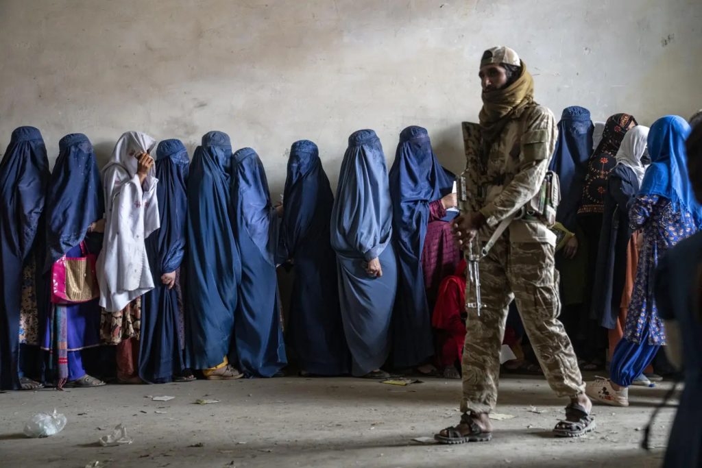 A Taliban fighter stands guard as women wait to receive food rations distributed by a humanitarian aid group at Kabul. AP/Ebrahim Noroozi