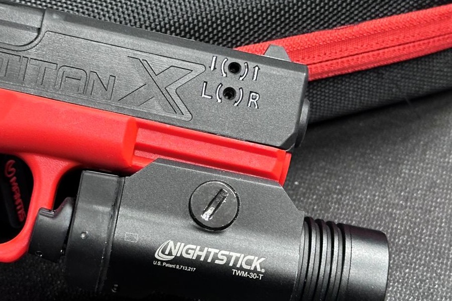 The end of an orange and black training pistol, showing two holes where it can be adjusted.