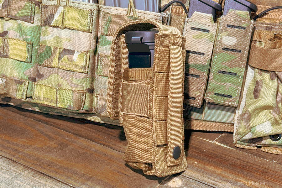A monocular in a dark brown, military style pouch in front of a camo vest. 