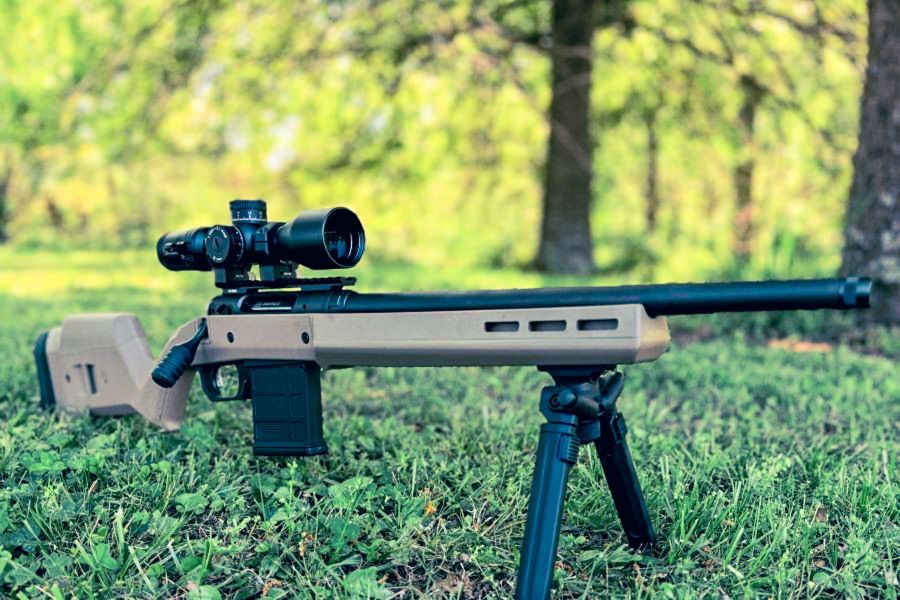 A brown rifle with a black scope, resting on a bi-pod in the green grass. German Precision Optics Centuri 4x16 Compact Scope
