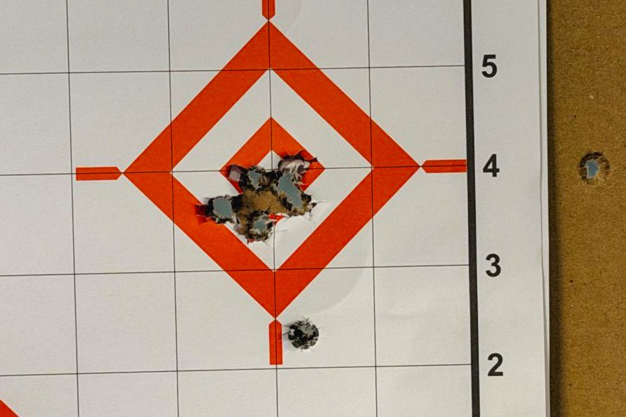 A white target with red lines in the center and several bullet holes in the center of the target and one bullet hole an inch below the bullseye. German Precision Optics Centuri 4x16 Compact Scope